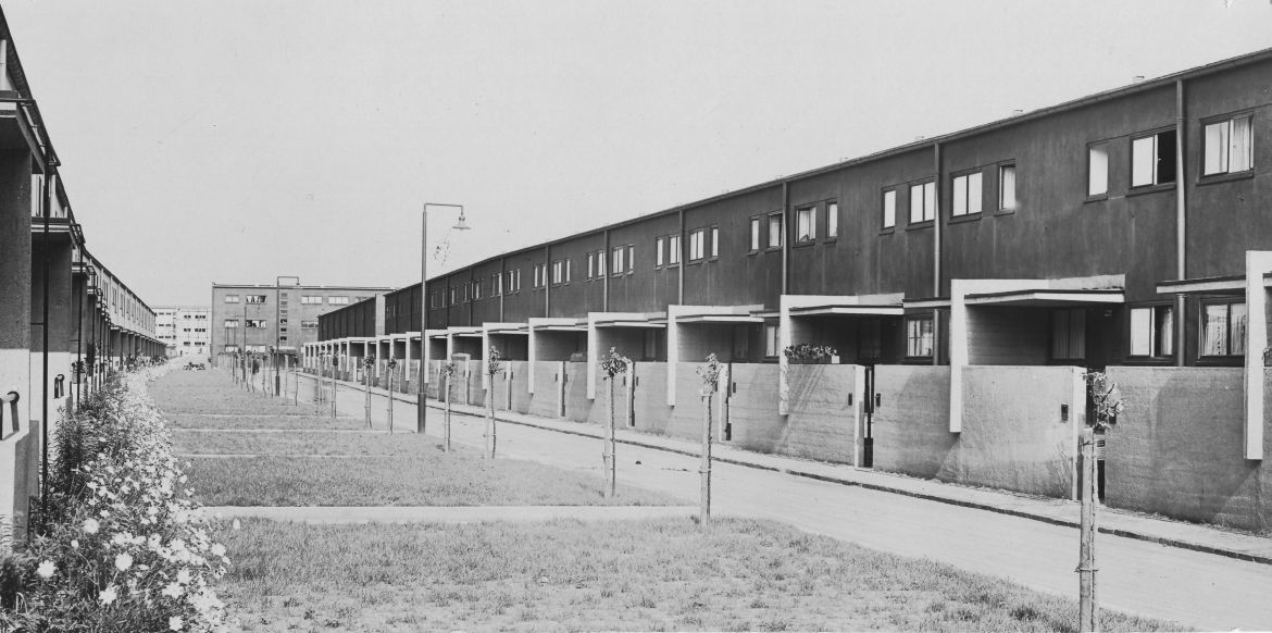 Siedlung Römerstadt, Frankfurt. Straße Im Burgfeld, Architekten: Ernst May mit Carl-Hermann Rudloff u. a., 1927-28, Fotograf: Max Göllner © Ernst-May-Gesellschaft, Frankfurt Schwarz-Weiß Fotografie einer Straße mit gleich aussehenden kleinen Reihenhäusern und Gärten mit Rasen