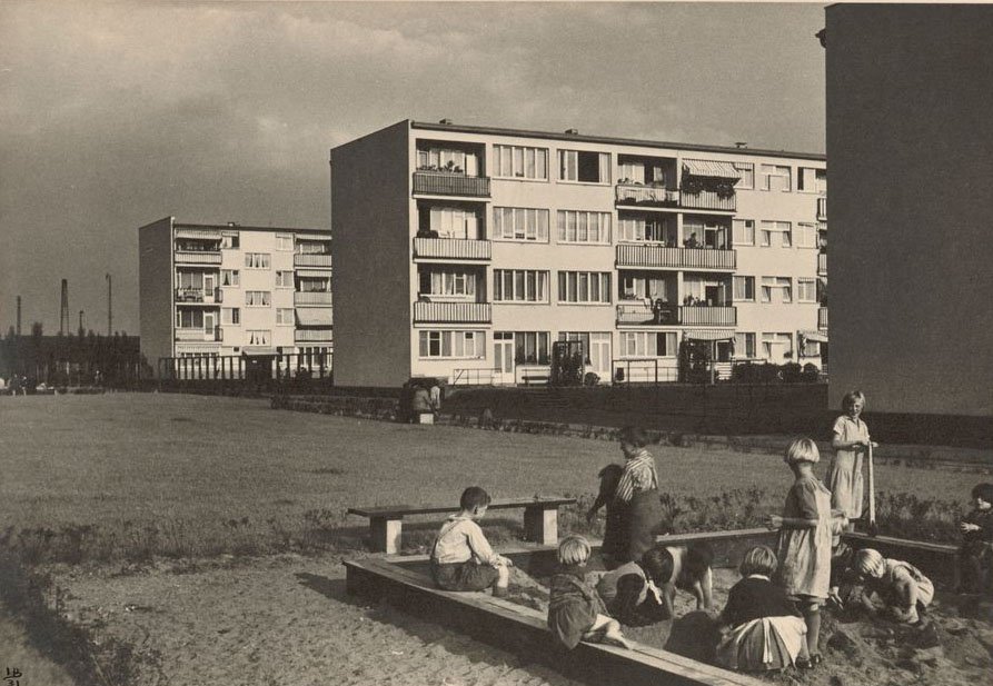 Ilse Bing, Serie „Hellerhofsiedlung“: Spielende Kinder, Frankfurt 1931, Canadian Center of Architecture, Inv.-Nr. PH2001: 0218 © Estate of Ilse Bing Schwarz-Weiß-Fotografie mit spielenden Kindern in einem Sandkasten im Vordergrund und Mehrfamilien-Siedlungshäusern im Hintergrund