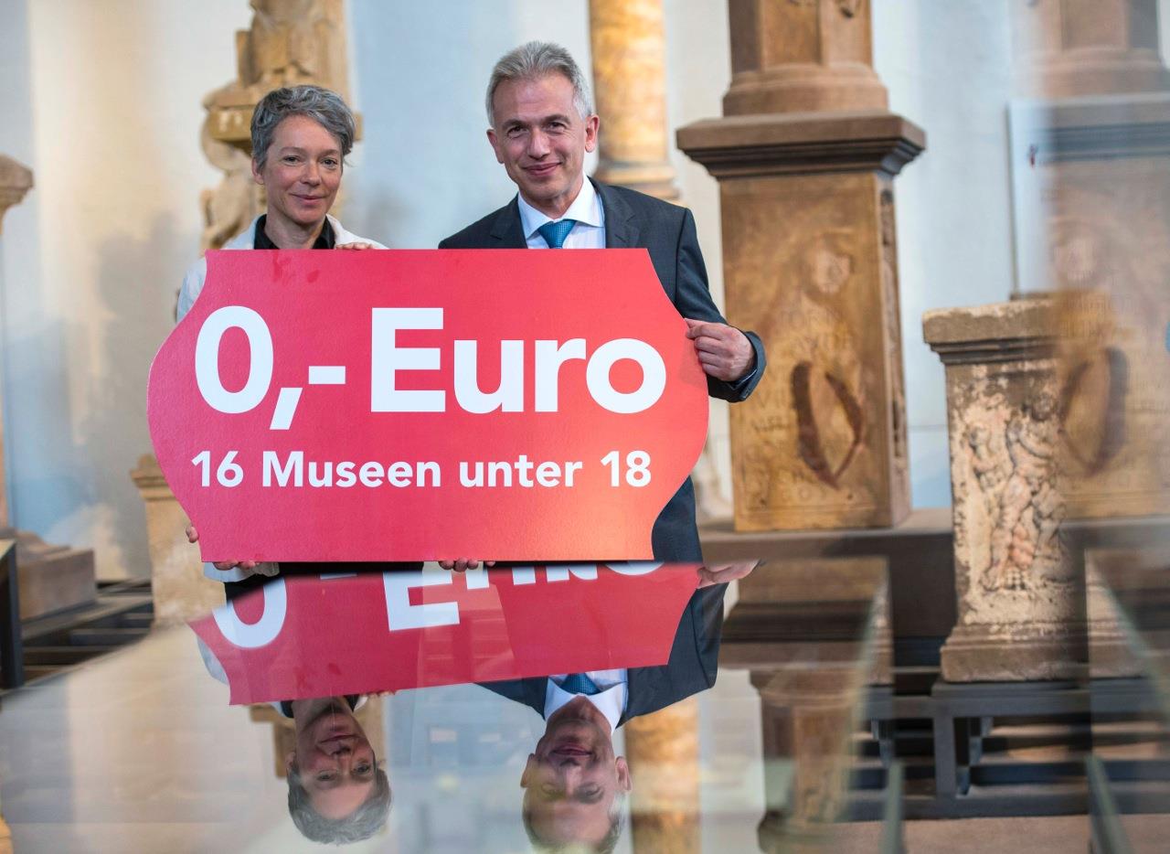 Die Kulturdezernentin und der Oberbürgermeister halten ein Plakat in der Hand, darauf der Text: Null Euro, 16 Museen unter 18 Jahre