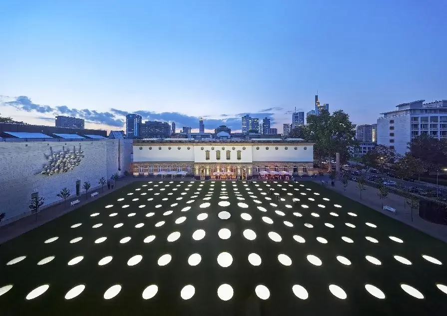 Städel Museum von hinten in den Abendstunden mit Städel Garten und den beleuchteten Oberlichtern des Ausstellungssaals unterhalb des Gartens und der Frankfurter Skyline im Hintergrund