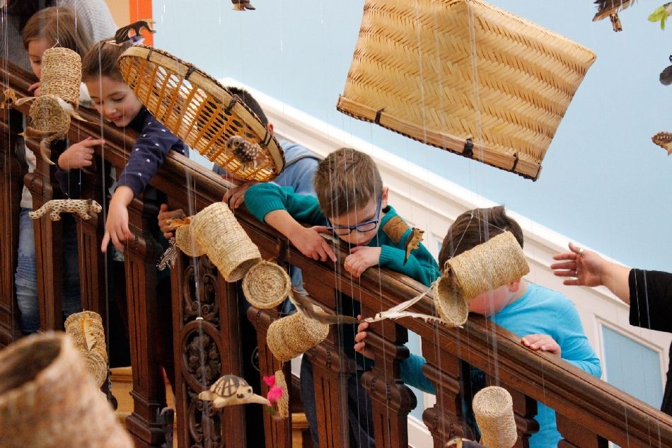 Kinder schauen von Treppengeländer im Weltkulturen Museum auf hängende Körbe von der Decke