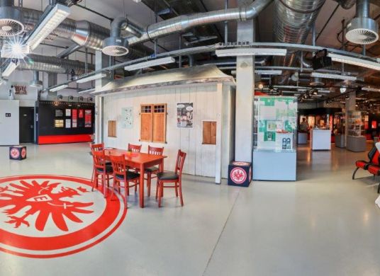 Foyer des Eintrachtmuseum mit Esstisch und Stühlen in der Mitte und hinten links einem Regal des Museumsshops