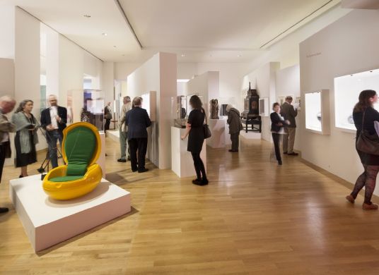 Besucher*innen in der Ausstellung des Museum Angewandte Kunst, modernes Sitzmöbel links im Vordergrund