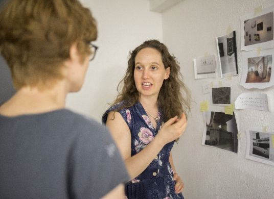 Zwei Frauen sprechen vor einer Wand mit angeheften Fotos und Notizen im Fotografie Forum