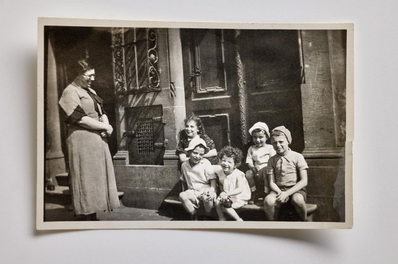 Die fünf Zuntz-Geschwister mit Mutter Ruth. Von links nach rechts: Esther, Leo, Mirjam, Harry und Simon © Familie Zuntz Auf einer alten Schwarz-Weiß-Fotografie schaut eine Frau auf fünf Kinder, die auf Treppenstufen vor einer Tür sitzen